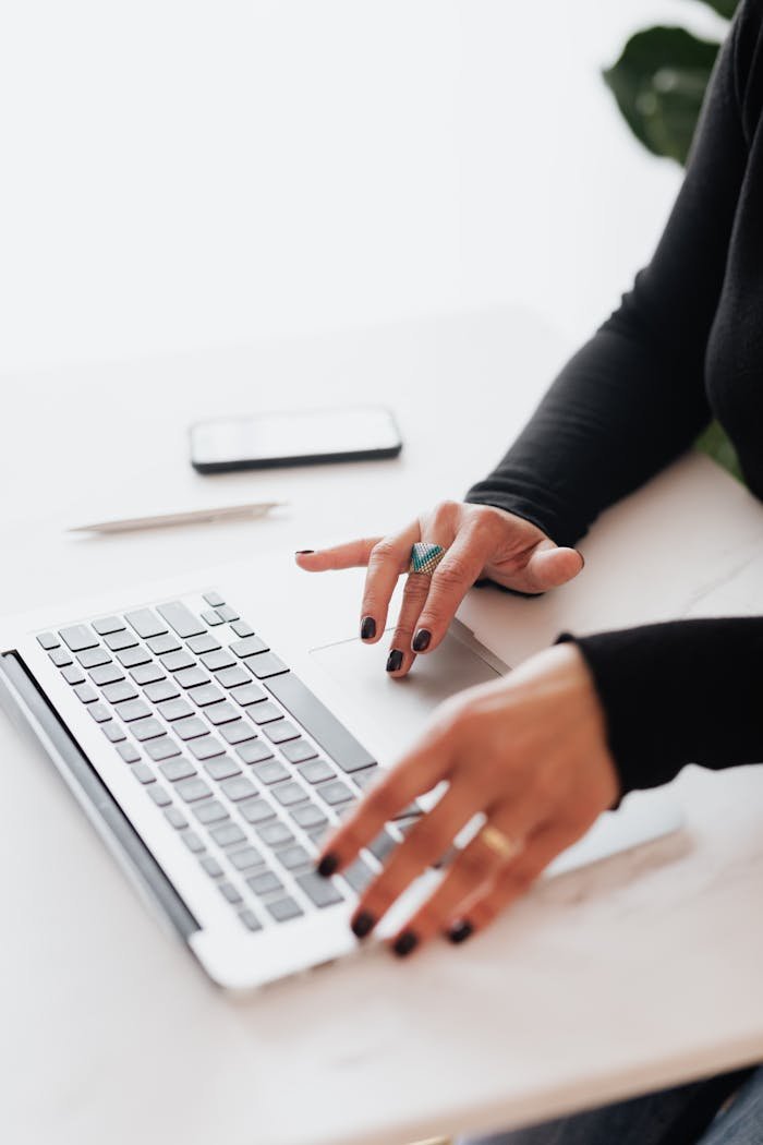 A businesswomans hands typing on a laptop at a bright, modern workspace.