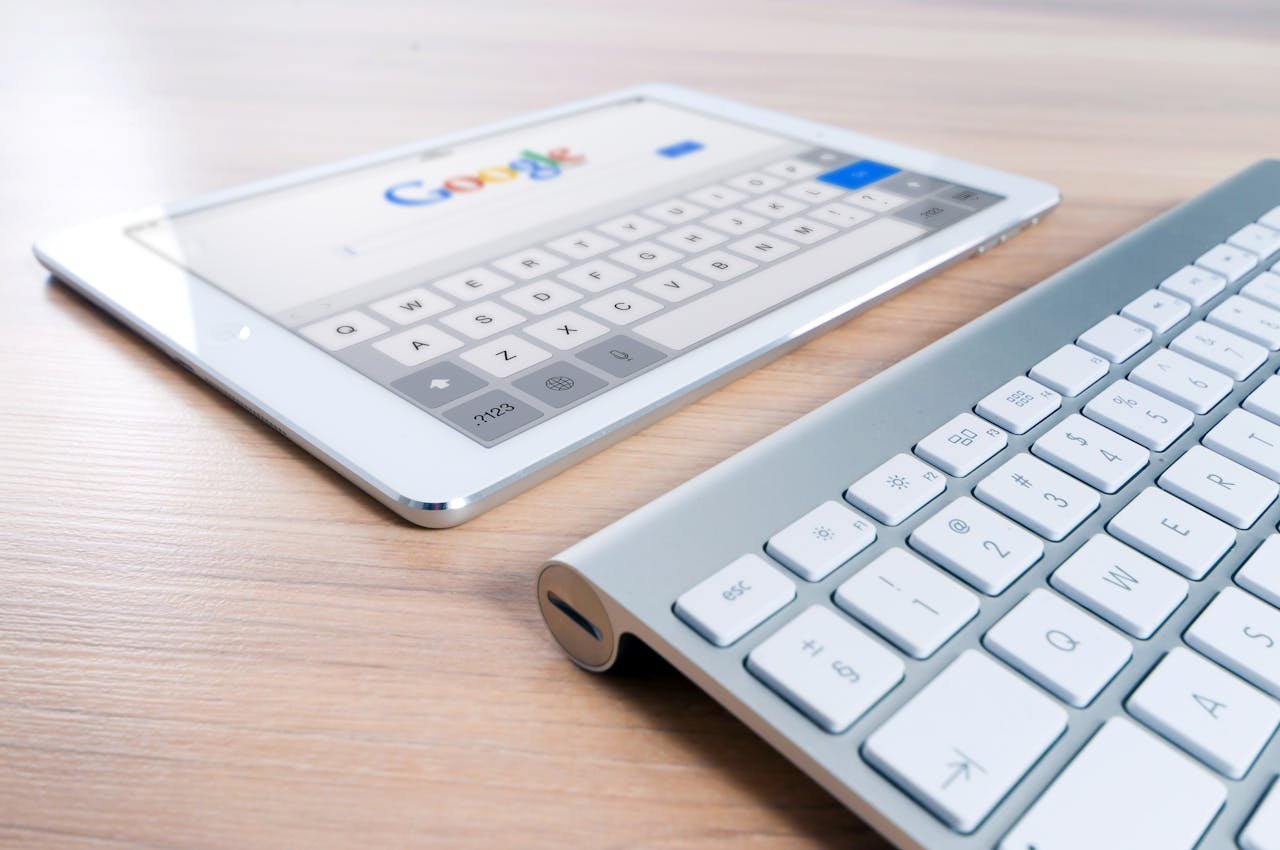 Home A modern tablet displaying a search engine logo next to a wireless keyboard on a wooden desk.